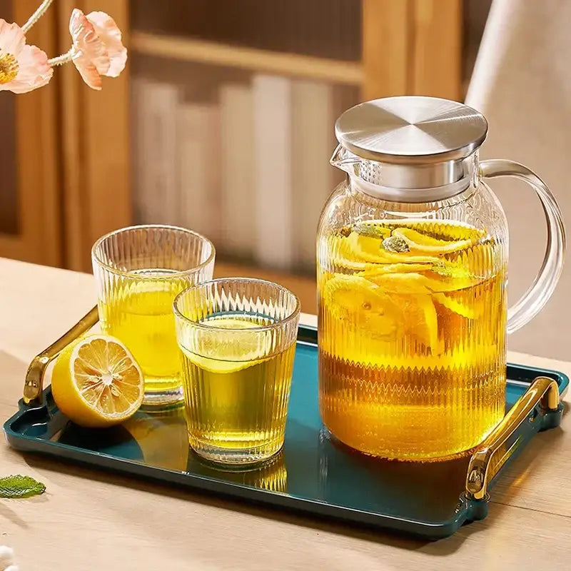 Modern striped glass cold water kettle set with silver lid filled with lemon-infused liquid in clear glass pitcher