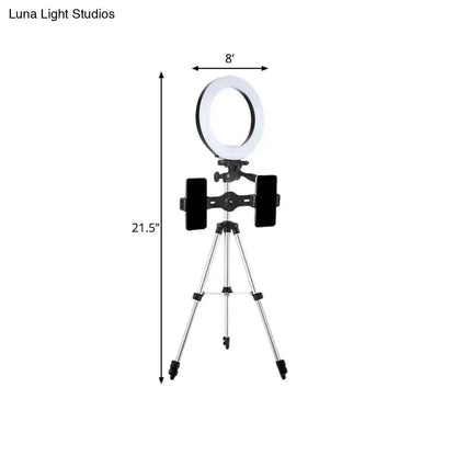 A modern style black and silver led flash light ring with white illumination mounted on a tripod with phone holders