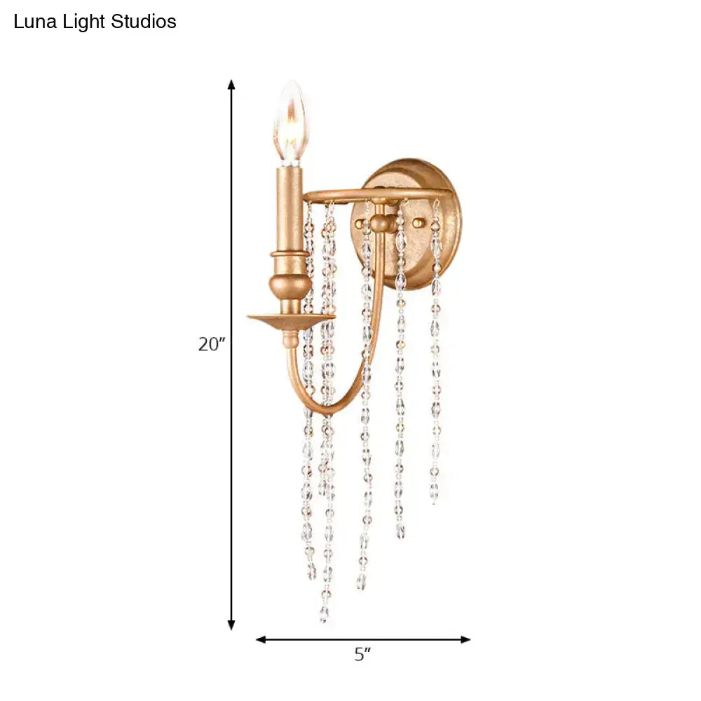 Modern style gold sconce with clear crystal beaded strand and single candle-style bulb for bedroom lighting