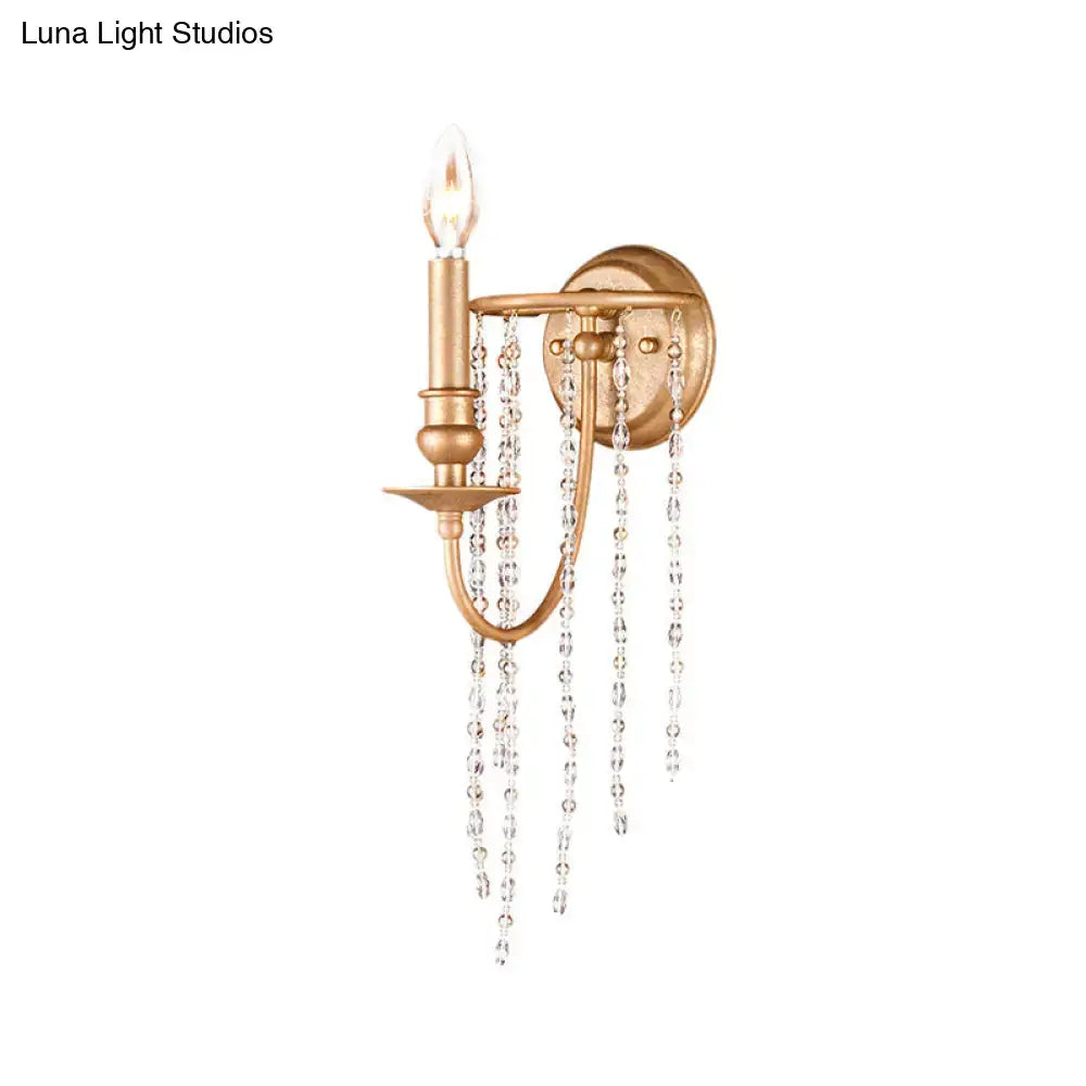 Modern style gold antique brass wall sconce with clear crystal beaded strand and single candle-style bulb for bedroom lighting
