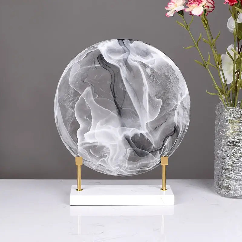 A translucent glass geometric disk with swirling black and white patterns on a white marble base home decor figurine