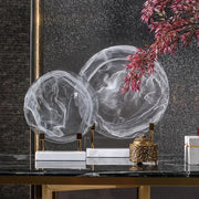 Two translucent swirling glass orbs with gold stands on white marble bases home decor figurines geometric disk design
