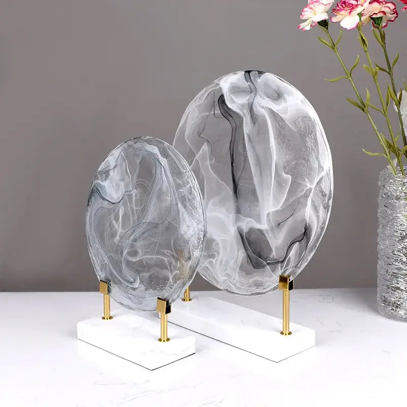 Two translucent oval glass sculptures with gray white marbled patterns on marble bases for home decor figurines