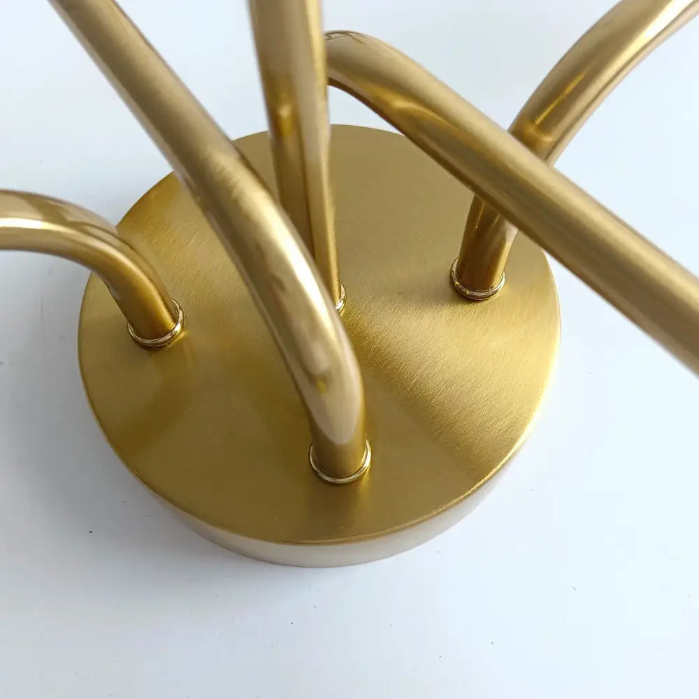Gold-toned metal coat rack with circular base and curved arms complements modern decorbites brass ceiling light design