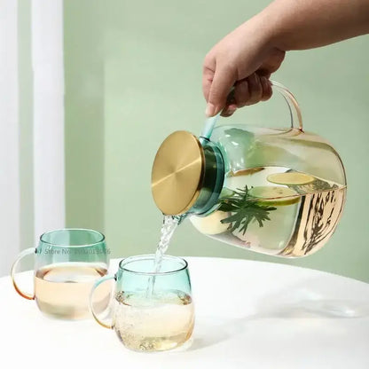 Clear glass teapot with gold-toned lid and handle filled with infused water in modern teal and gold glass teapot set