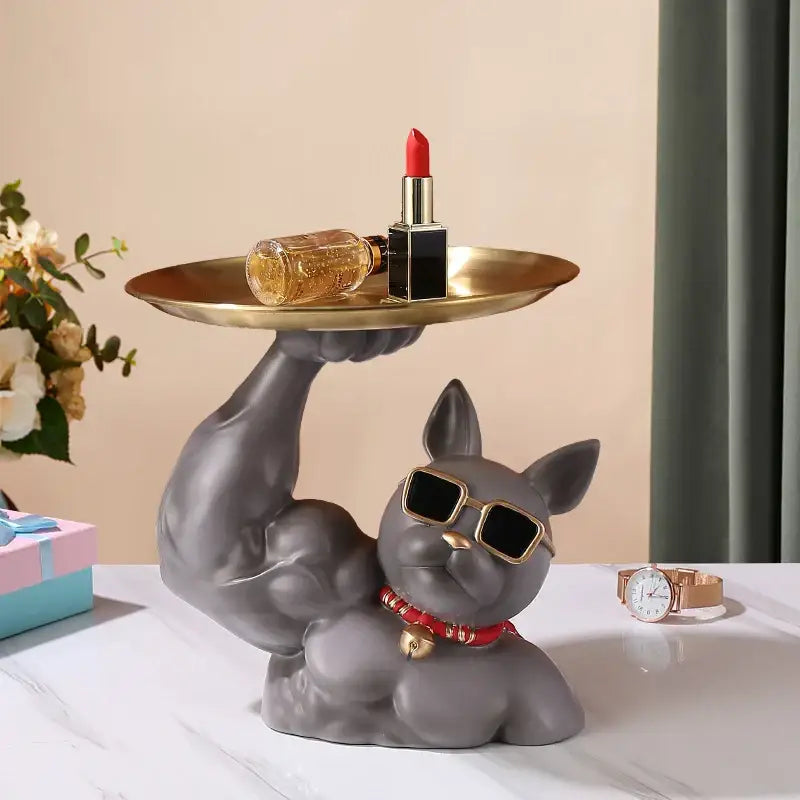 Gray ceramic decorbites bulldog tray with muscular arms wearing gold-rimmed sunglasses and red beaded collar holding golden tray