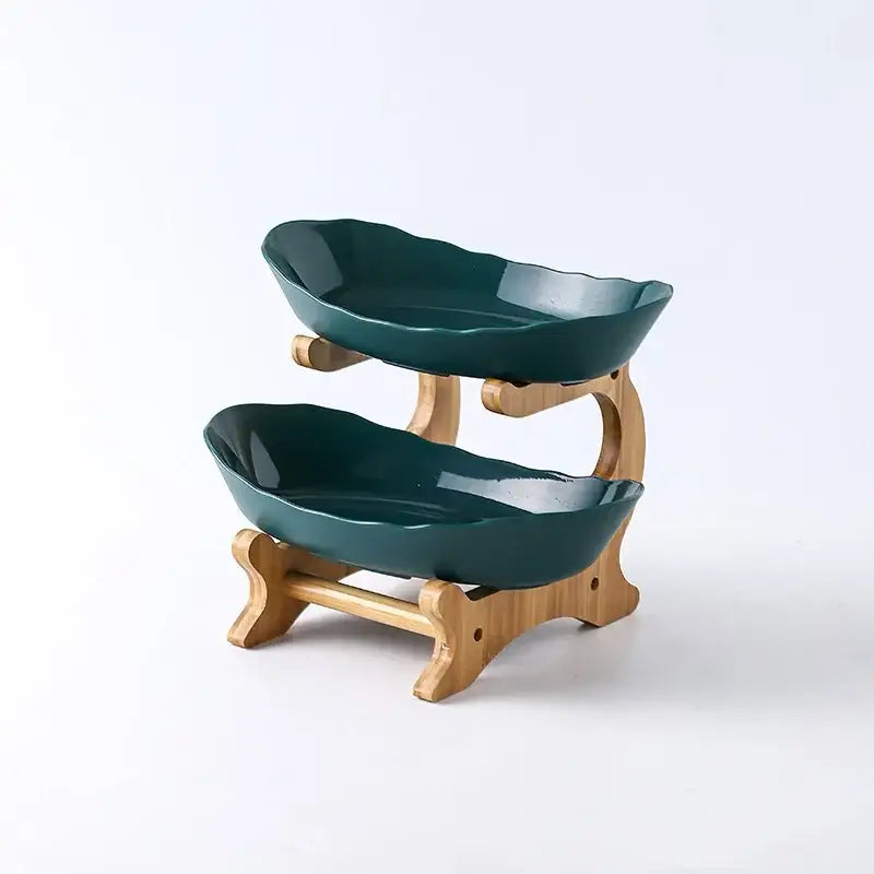 Two-tiered modern teal and white ceramic layer table plates with leaf-shaped bowls on a light wood stand for dining room use