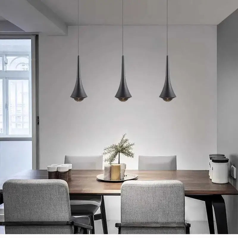 Three matte black conical pendant lights with black cords hang above a wooden dining table in modern dining room
