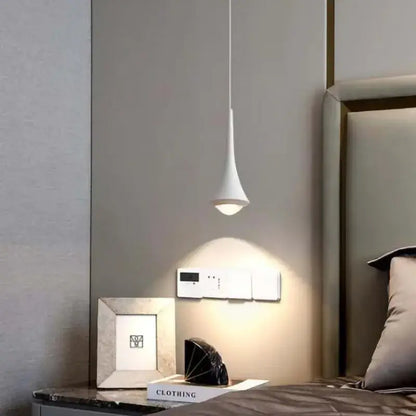 A sleek white teardrop pendant light with a gold black and white cord pendant light design above a bedside table