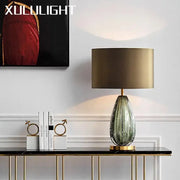 A sleek teardrop textured green and gold glass table lamp on a modern console table for bedroom decorbites use