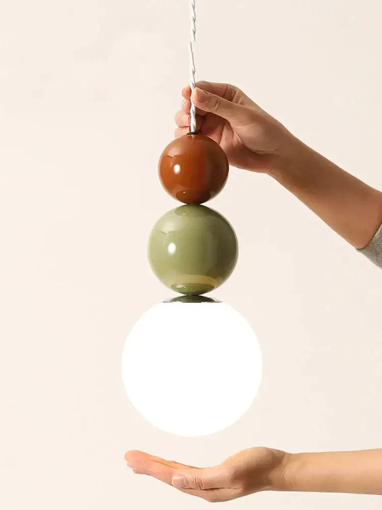 A modern pendant light with glossy terracotta and sage green ceramic spheres and a glowing white glass globe