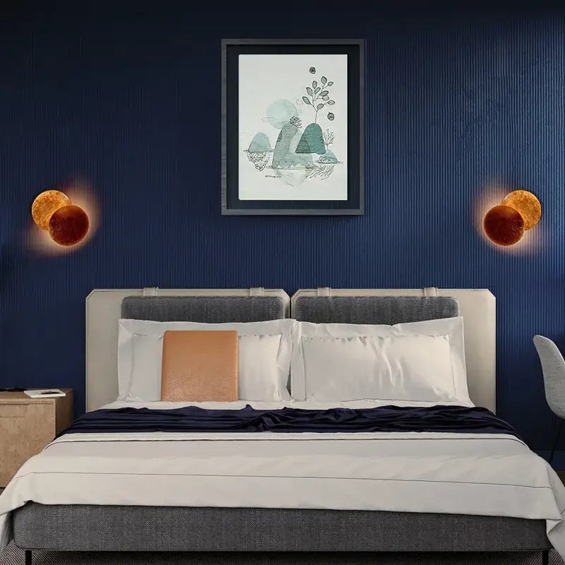 The modern textured eclipse round wall lamp features a gray upholstered headboard and white bedding with an orange pillow
