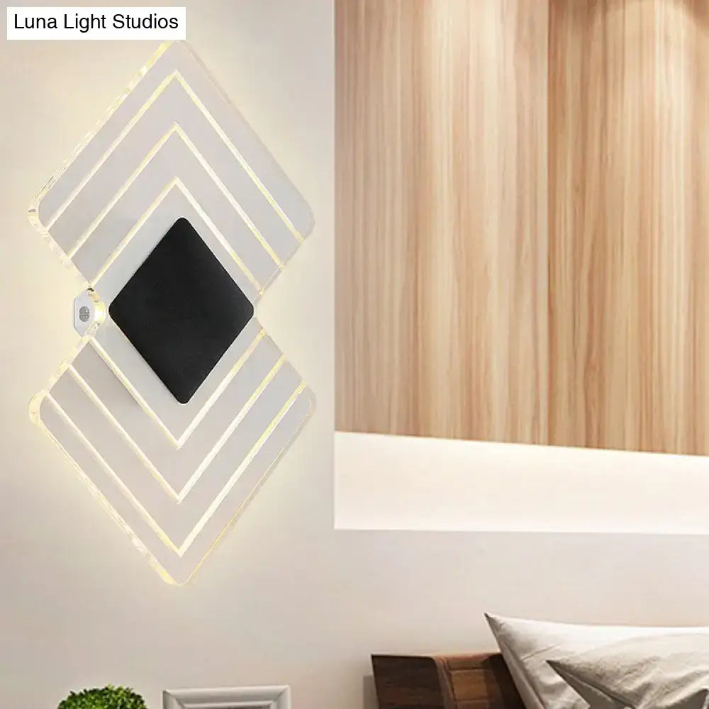 Modern textured silver and black direct wired electric wall sconce with layered acrylic panels emitting warm light