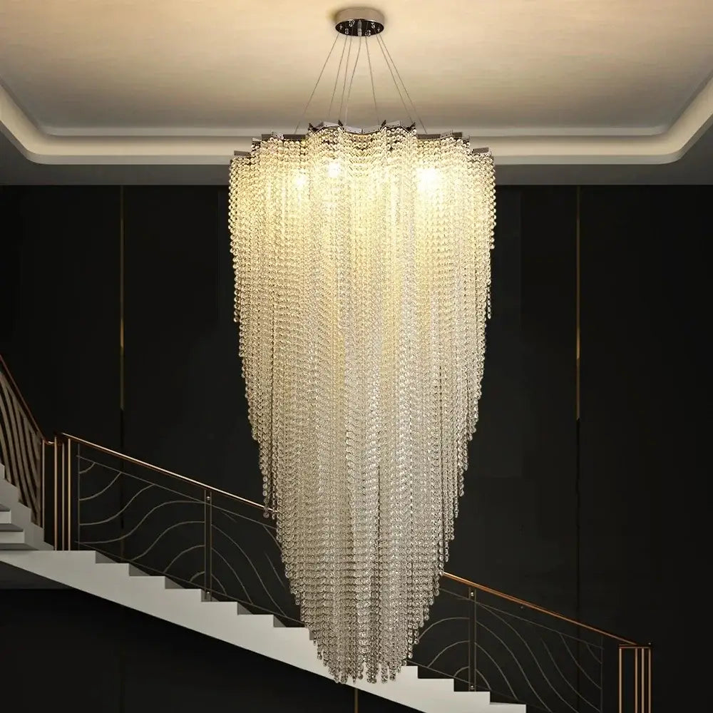 A modern tiered decorbites colorful crystal chandelier with cascading crystals hangs from a staircase ceiling