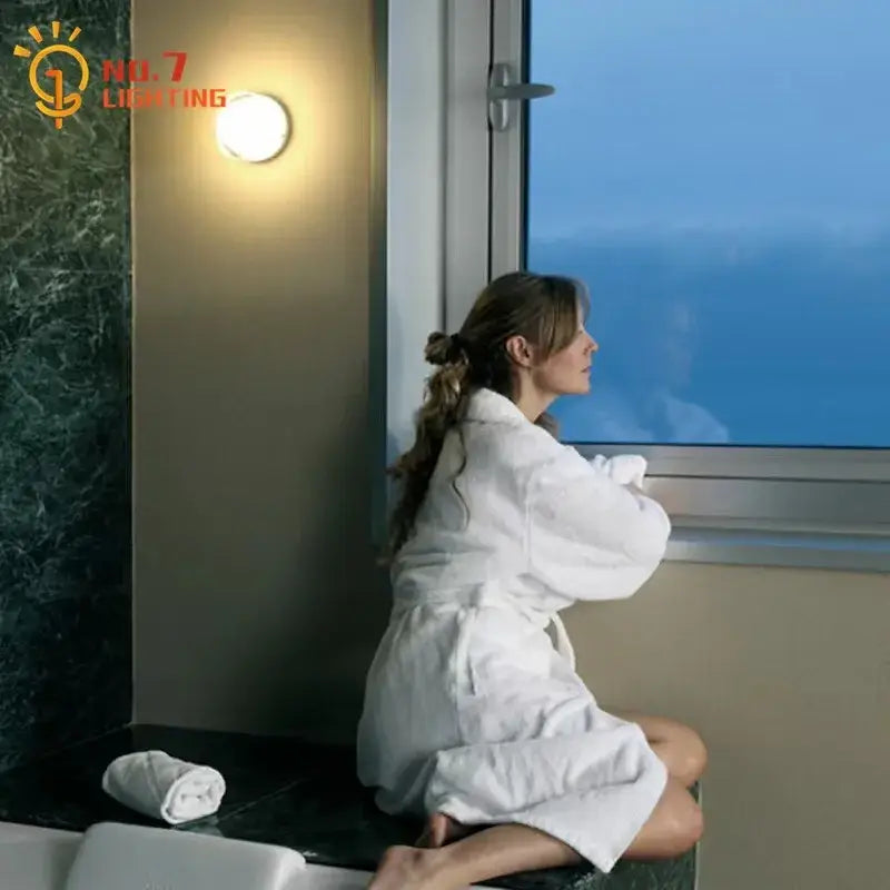 Woman in white plush robe sitting by bathtub next to modern translucent glass dimple potato chip wall lamp