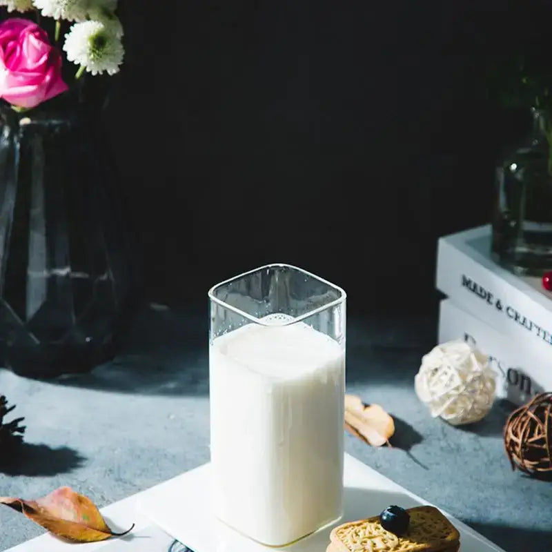 A modern transparent glass square cup filled with white milk on a white plate for kitchen and dining use
