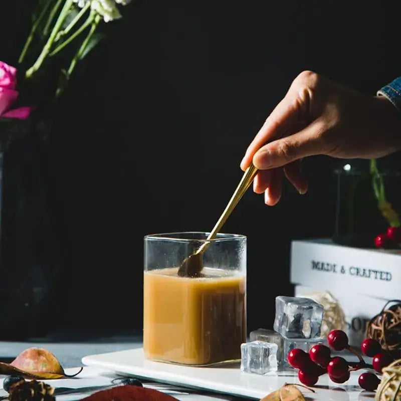 Modern transparent glass square measuring cup with golden spoon stirring iced coffee in a transparent glass cup