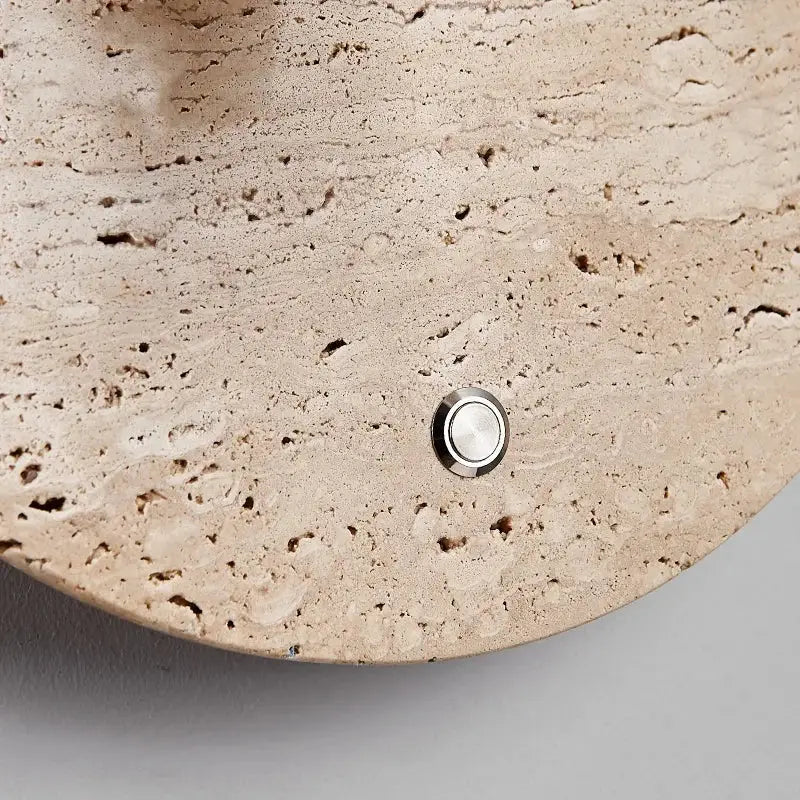 A sleek circular silver doorbell button on textured beige stone complements modern travertine decorbites led wall light