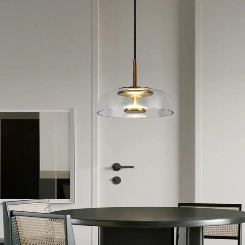 Modern tricolor glass pendant light with clear glass dome and brass accents hanging in a dining room pendant light