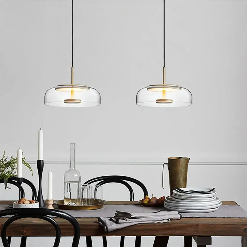Two modern tricolor glass pendant lights with brass accents hang above a dining room table