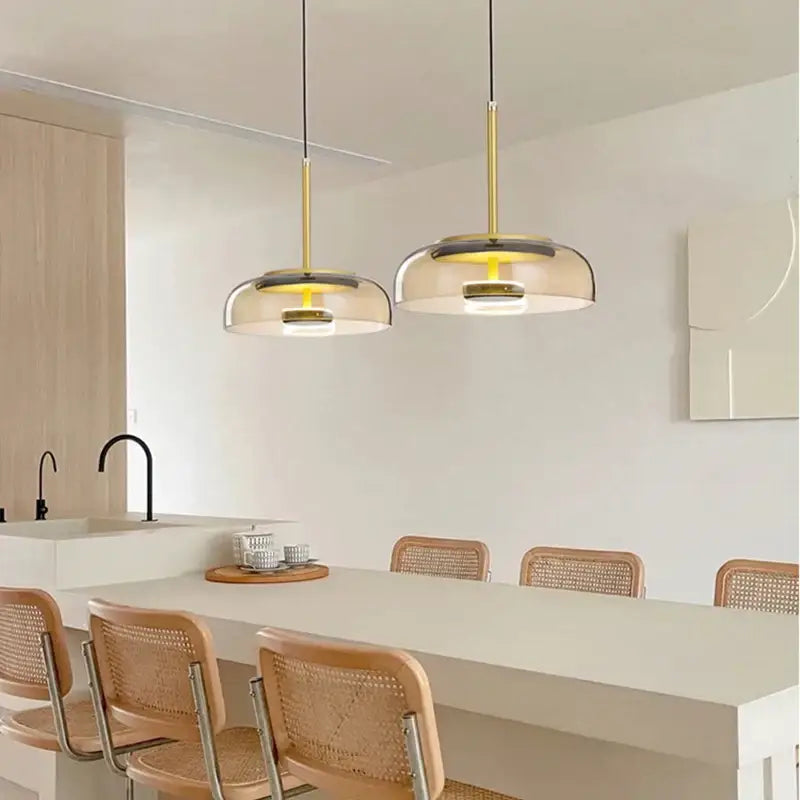 Two modern pendant lights with gold metal stems and translucent glass pendant shades hang over a white dining room table