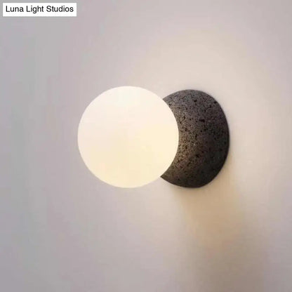Minimalist wall lamp with white glass spherical globe on dark volcanic stone base for living room inch fixture