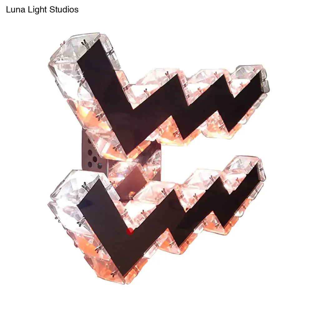 Modern w-shaped beveled crystal wall lamp with translucent panels and black frame emitting warm orange LED light