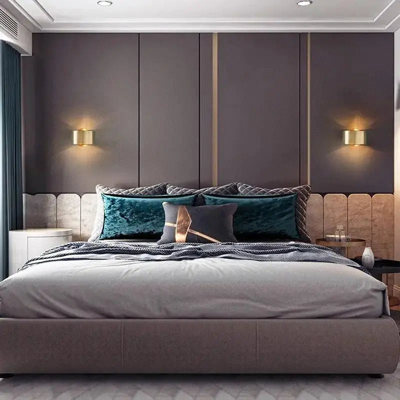 A modern wall lamp in black gold mounted above a plush gray velvet bedspread with a textured quilted edge