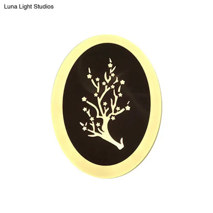 An oval decorative plaque with a black center and white tree design framed by gold complementing a white acrylic wall lamp