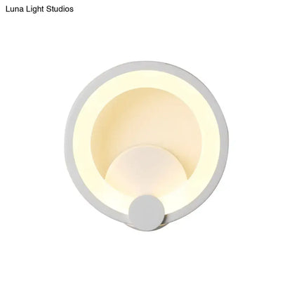 Modern white acrylic sconce light with circular concentric ring design emitting warm ambient light for bedroom use