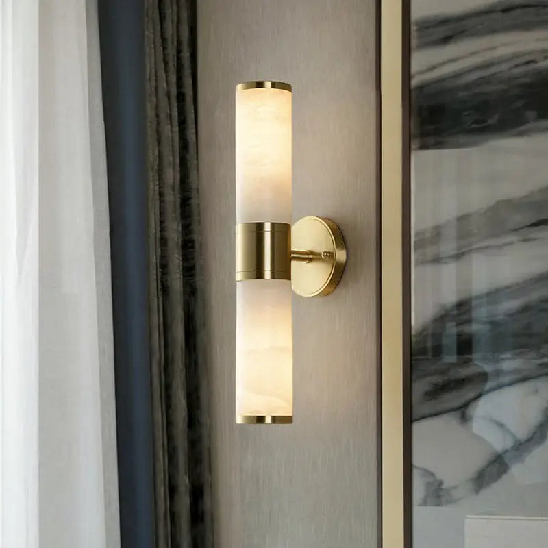 Modern white and brass pillar shaped sconce light with gold-toned cylindrical frosted glass shade for bedside wall lamp use