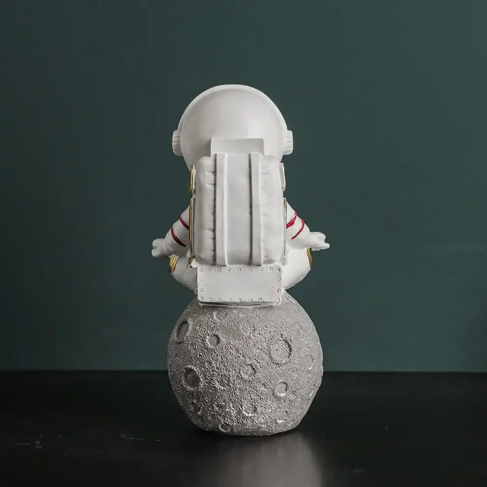 Modern white astronaut figurine with red stripes sitting meditative on textured gray moon electroplated golden decor