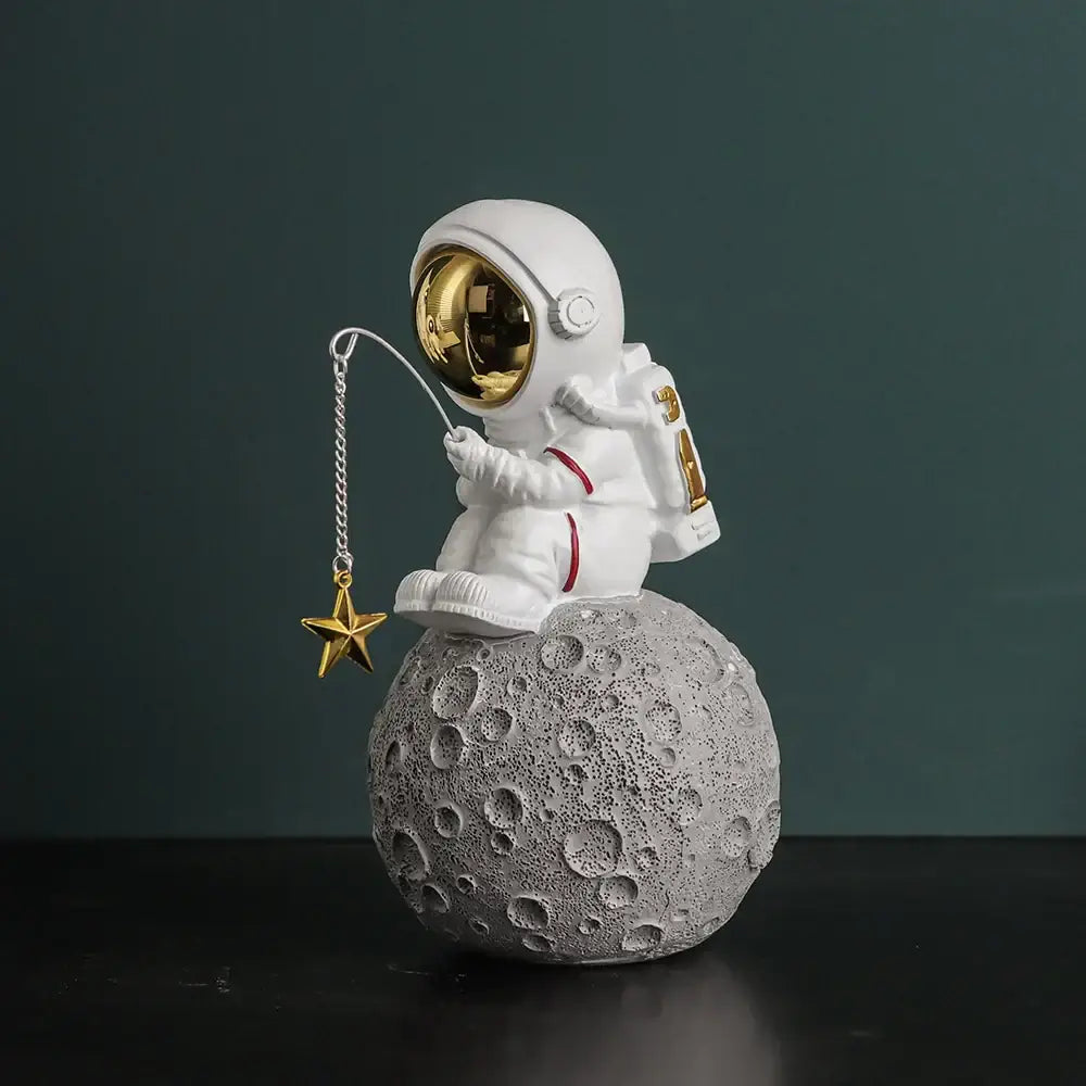 Modern white and electroplated golden astronaut figurine sitting on gray moon surface holding golden star fishing lure for decor