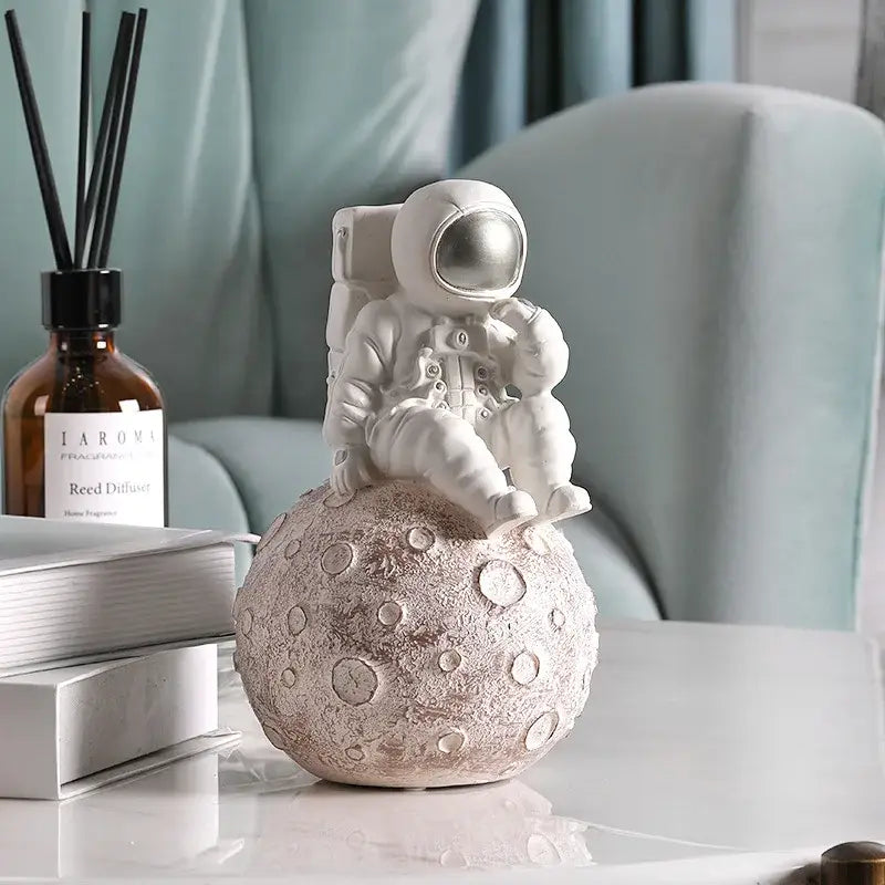 Modern white and gold astronaut phone holder figurine sitting atop a textured cratered moonbase for decorbites astronaut phone decor