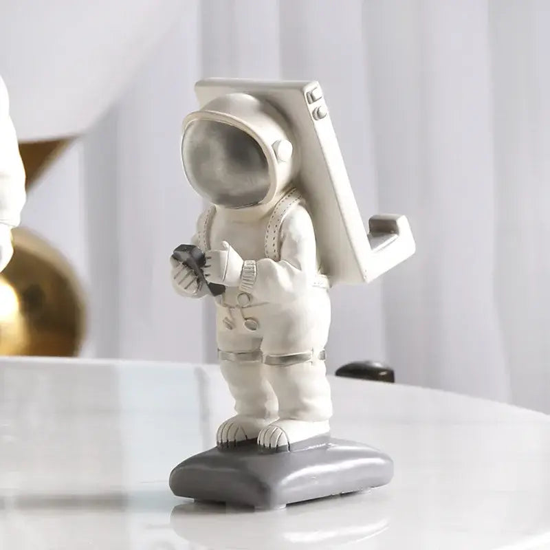 Modern white and gold decorbites astronaut phone holder figurine with metallic silver helmet standing on gray base