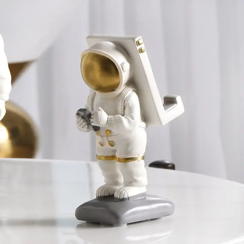 Modern white and gold astronaut phone holder figurine with a gold visor standing on a gray base for decorbites astronaut phone decor