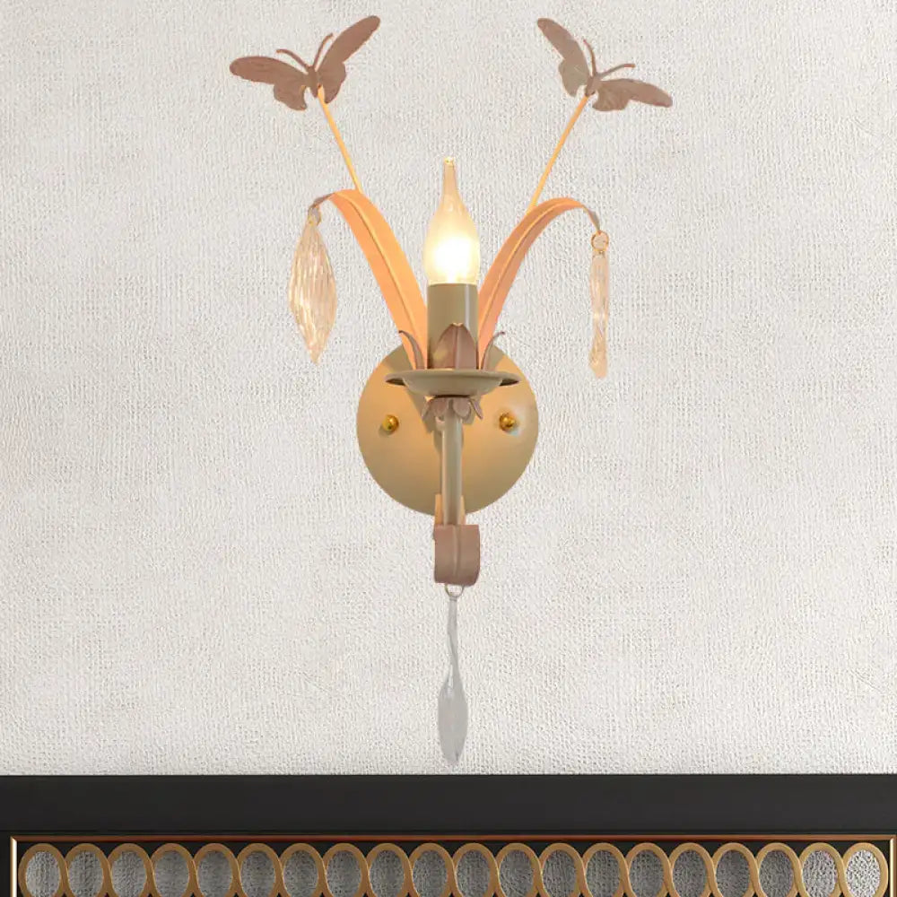 A delicate peach-toned metal wall lamp with white finish butterfly motifs and crystal accents for home décor