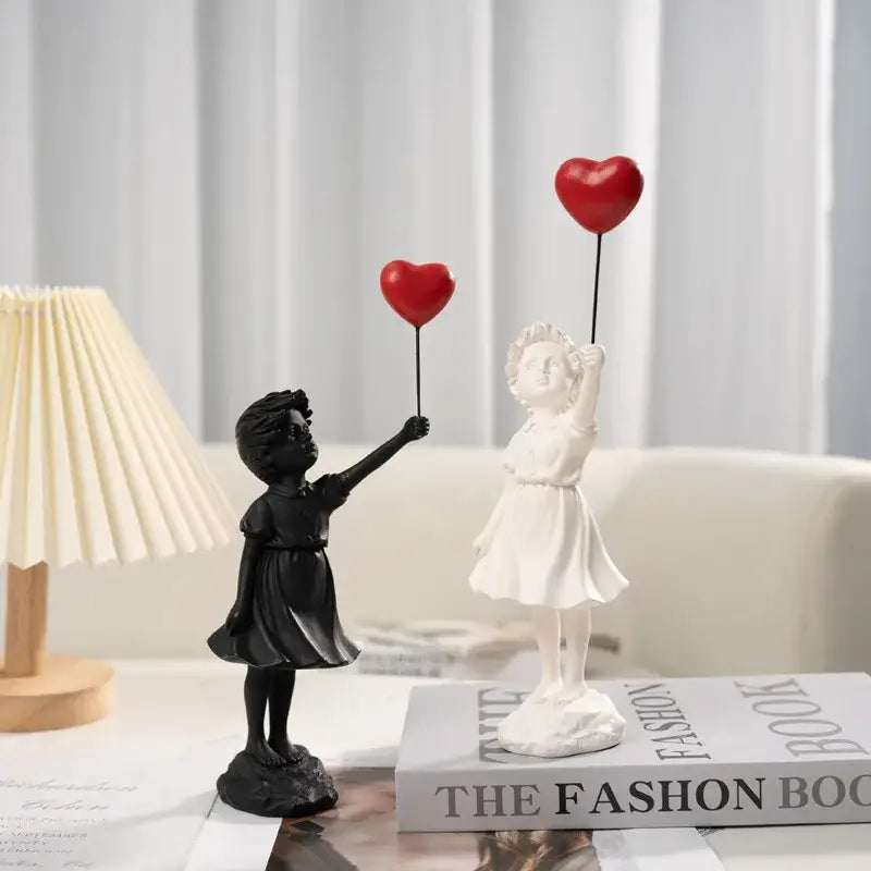 Modern white and red banksy girl balloon sculpture featuring black and white resin figurines holding red heart balloons