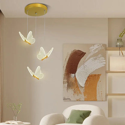 Three white butterfly pendant lights with warm gold finish hang from a circular warm gold ceiling fixture