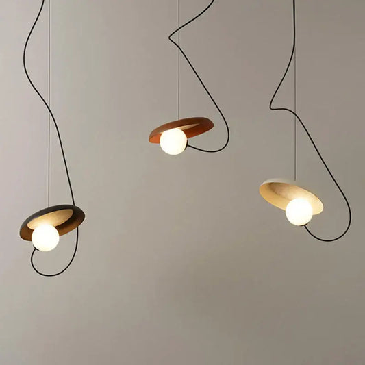 Three modern pendant lights with metal finish feature curved black cords and circular wooden shades for dining room use