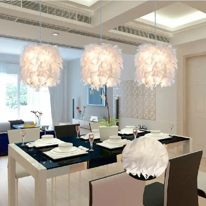 Three elegant white feather pendant lights hang above a modern dining table in a white and black bedroom cloud design