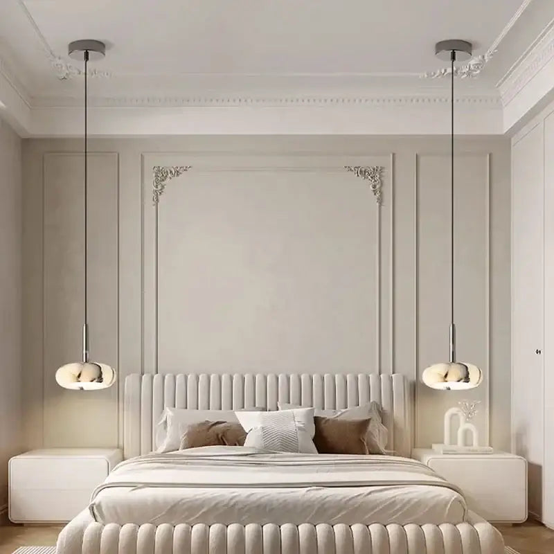 Cream-colored tufted bed with plush headboard and footboard featuring a modern white marble bedside pendant light