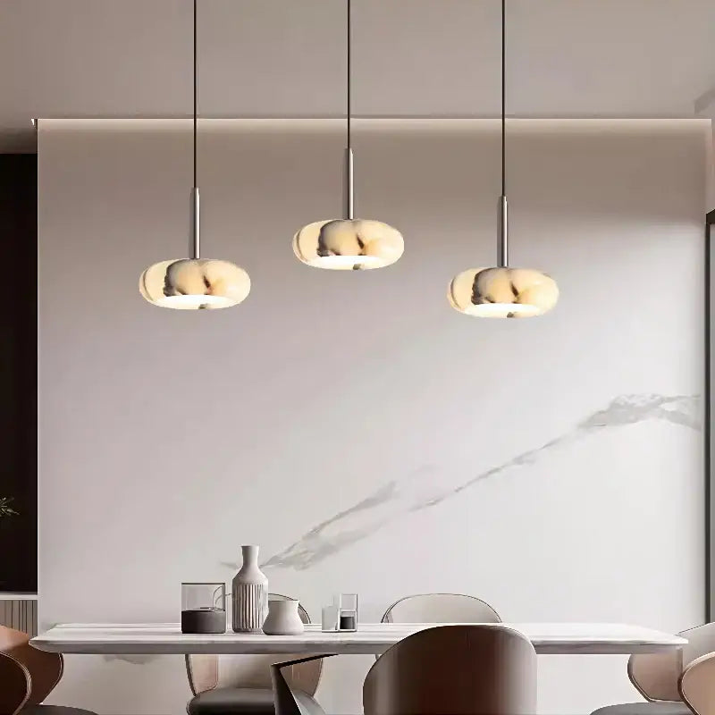 Three modern bedside pendant lights with smooth white marble shades and slender metallic rods for bedroom use