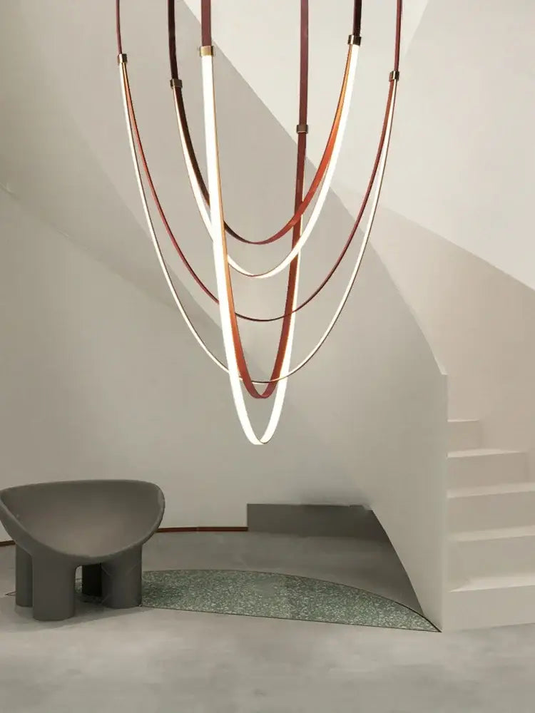 A modern white and brown leather chandelier with curved illuminated tubes in a sculptural belt pendant light design