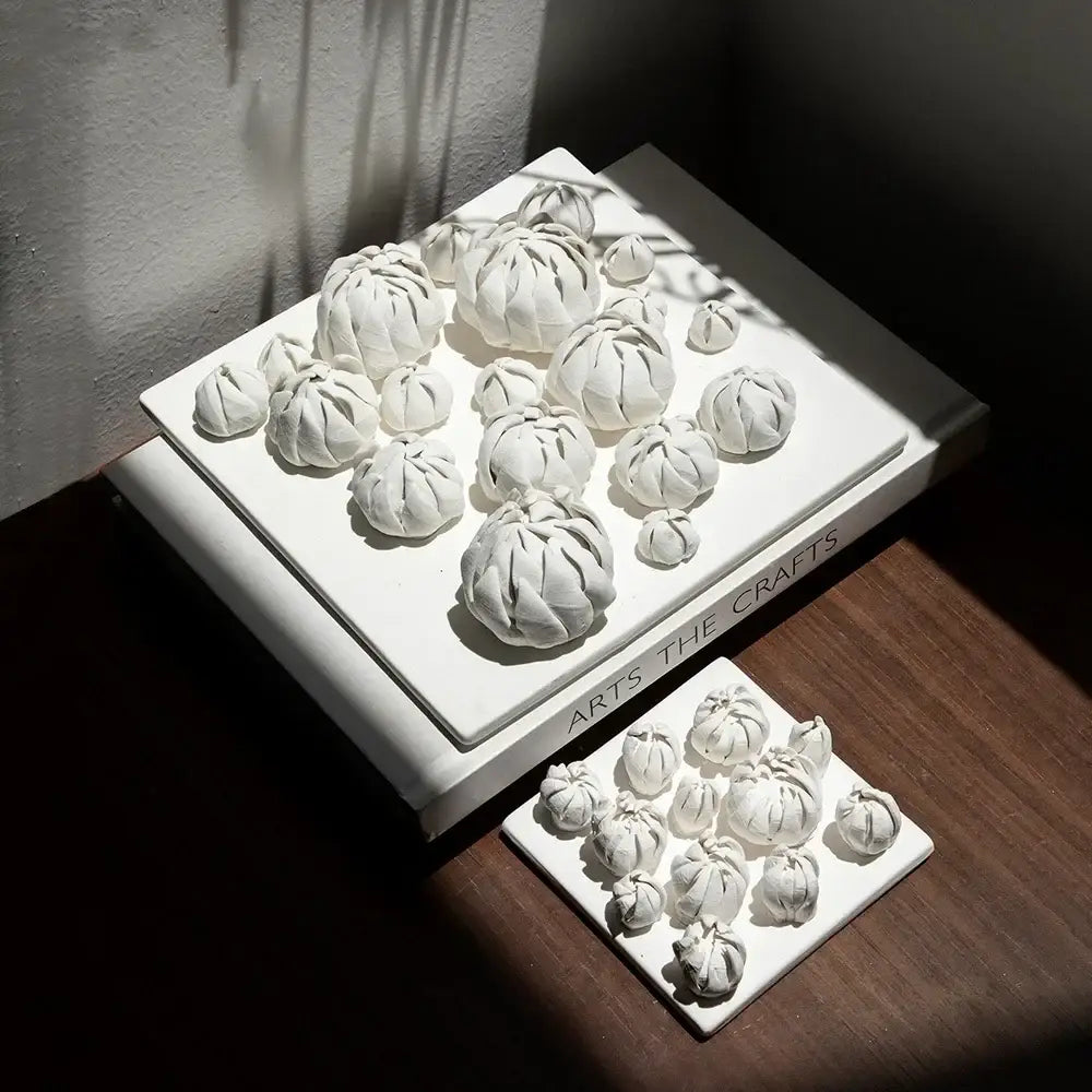 Modern white bud ceramic wall décor pendant featuring white ceramic sculptures resembling bundled fabric on platters