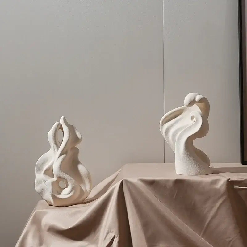 Two modern white ceramic curl sculptures with flowing organic forms on a beige draped tablecloth for decor