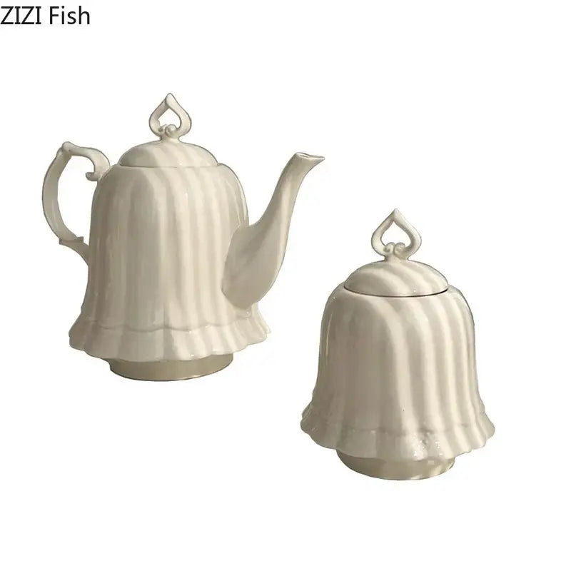 Cream-colored porcelain teapot and sugar bowl set with vertical stripes and heart-shaped finials beside ceramic tissue box with camellia flower