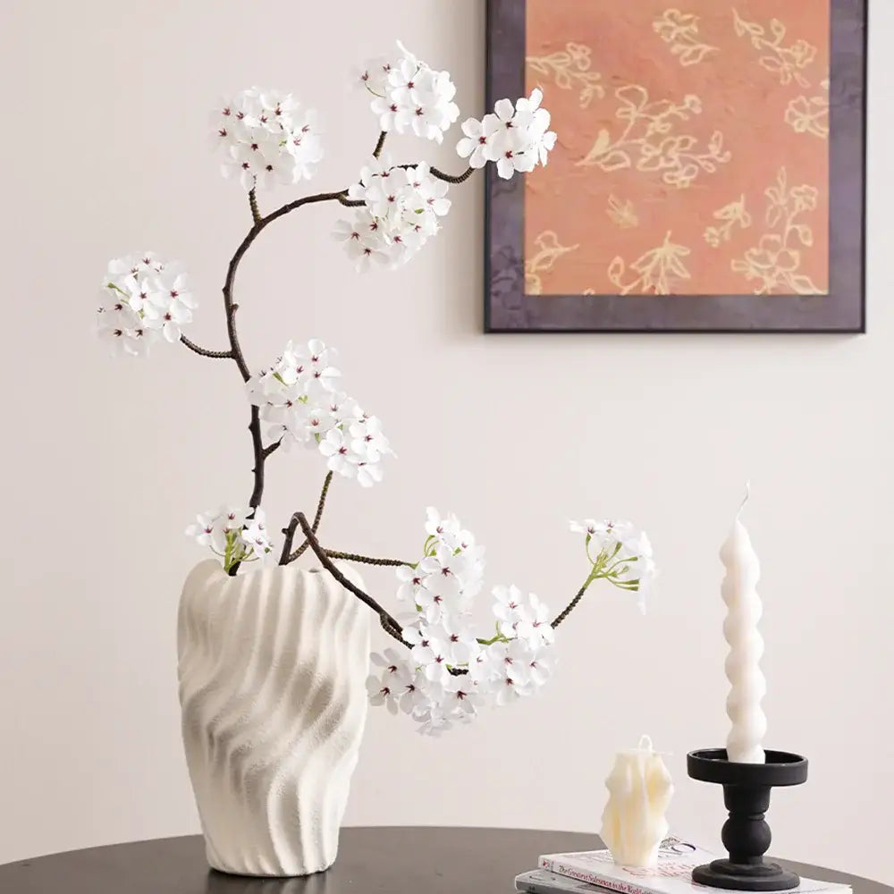 Modern white ceramic vase with irregular wavy patterns holding delicate artificial cherry blossoms for living room decor