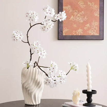 Modern white ceramic vase with irregular wavy patterns holding delicate artificial cherry blossoms for living room decor