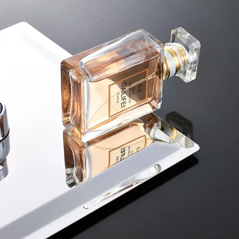 A rectangular glass perfume bottle with gold accents next to a modern white chrome square rainfall shower head fixture